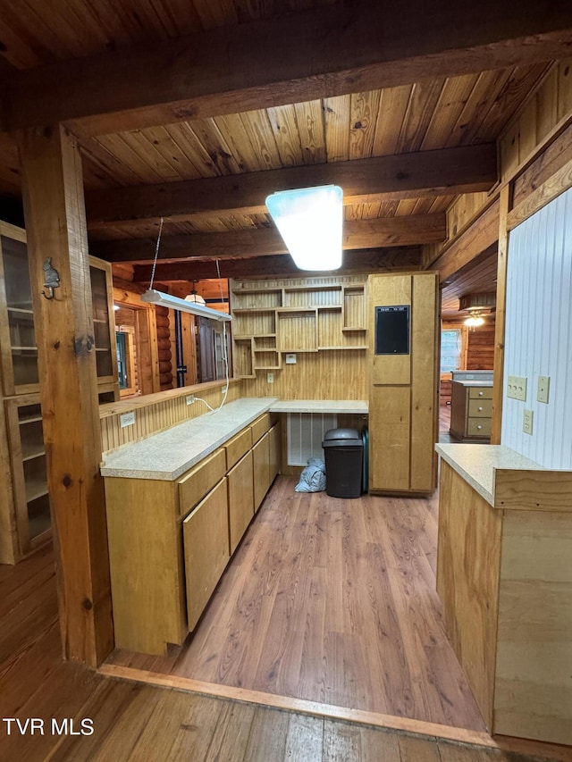 kitchen featuring kitchen peninsula, beam ceiling, light wood-type flooring, and wooden walls