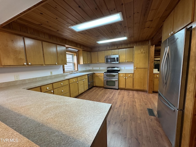 kitchen with kitchen peninsula, appliances with stainless steel finishes, light wood-type flooring, sink, and wooden ceiling