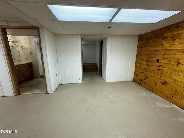 basement featuring wooden walls and a drop ceiling