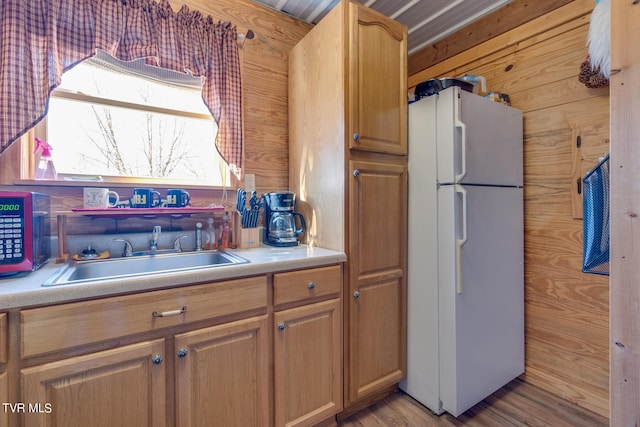 kitchen featuring light hardwood / wood-style flooring, wood walls, white fridge, and sink