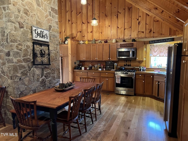 kitchen featuring high vaulted ceiling, hanging light fixtures, hardwood / wood-style flooring, appliances with stainless steel finishes, and beam ceiling