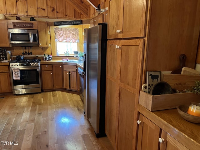 kitchen with vaulted ceiling, stainless steel appliances, and light hardwood / wood-style flooring