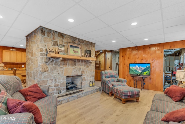 living room featuring hardwood / wood-style flooring, a stone fireplace, a drop ceiling, and wood walls