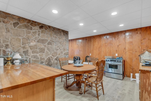 dining space with a paneled ceiling, wooden walls, and light hardwood / wood-style flooring