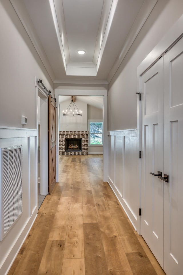 hall featuring a barn door, light hardwood / wood-style floors, a tray ceiling, and an inviting chandelier