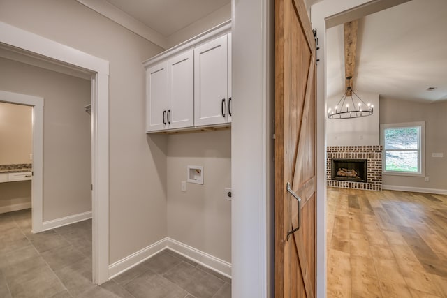 laundry area featuring a fireplace, a barn door, cabinets, hookup for an electric dryer, and a chandelier