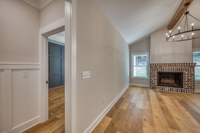 unfurnished living room featuring lofted ceiling with beams, a brick fireplace, a notable chandelier, and light hardwood / wood-style flooring