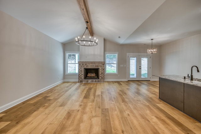 unfurnished living room featuring beamed ceiling, a brick fireplace, light hardwood / wood-style floors, a chandelier, and french doors