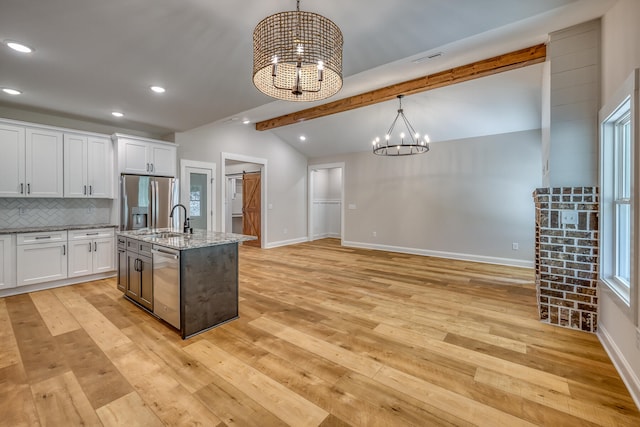 kitchen featuring pendant lighting, light stone counters, light hardwood / wood-style floors, white cabinetry, and a center island with sink