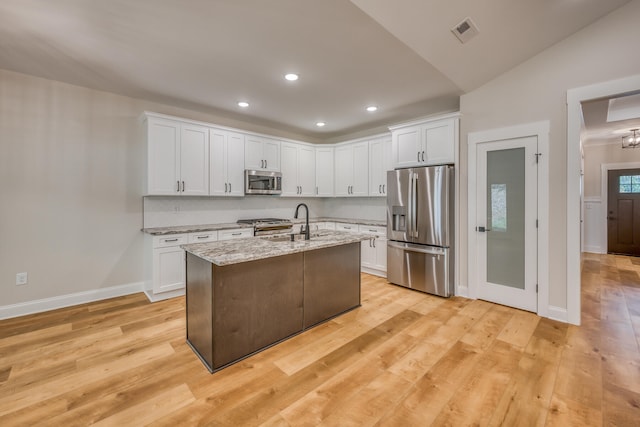 kitchen with appliances with stainless steel finishes, white cabinetry, an island with sink, and light hardwood / wood-style flooring