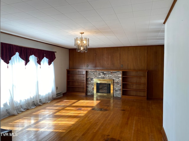 unfurnished living room featuring built in shelves, wooden walls, light hardwood / wood-style flooring, and an inviting chandelier