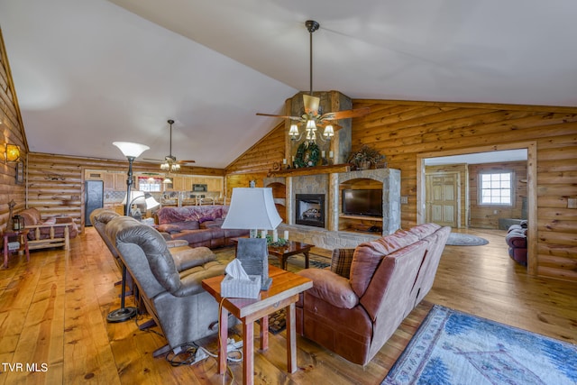 living room featuring a stone fireplace, light hardwood / wood-style floors, rustic walls, high vaulted ceiling, and ceiling fan