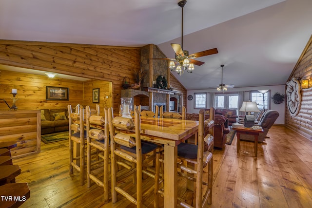 dining area featuring wood walls, hardwood / wood-style floors, ceiling fan, and vaulted ceiling