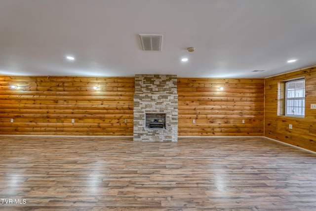 unfurnished living room featuring a fireplace, wood-type flooring, and rustic walls