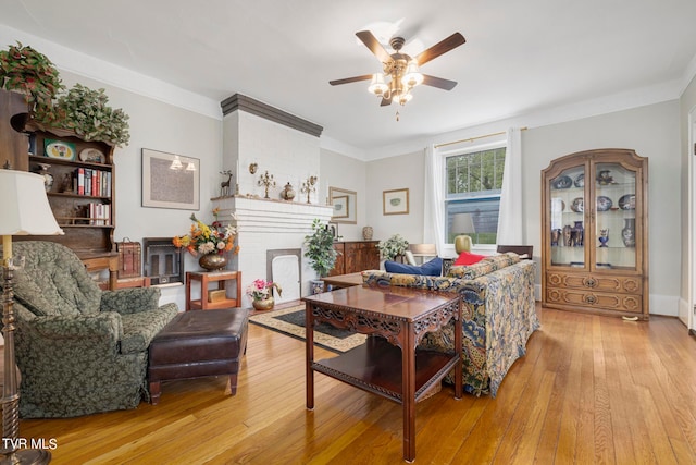 living room with crown molding, a fireplace, ceiling fan, and light wood-type flooring