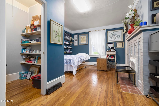 bedroom featuring hardwood / wood-style floors, crown molding, and a brick fireplace