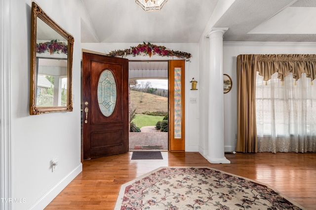 foyer entrance with light hardwood / wood-style floors, decorative columns, and lofted ceiling