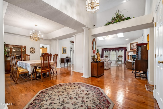 dining area with a high ceiling, hardwood / wood-style floors, a chandelier, and decorative columns