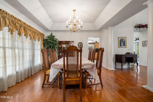 dining area with a raised ceiling, light hardwood / wood-style floors, a notable chandelier, and a healthy amount of sunlight