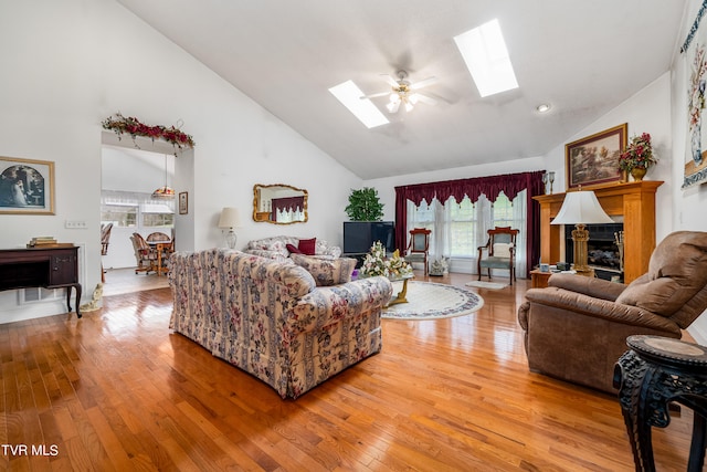 living room with ceiling fan, high vaulted ceiling, light hardwood / wood-style floors, and a skylight