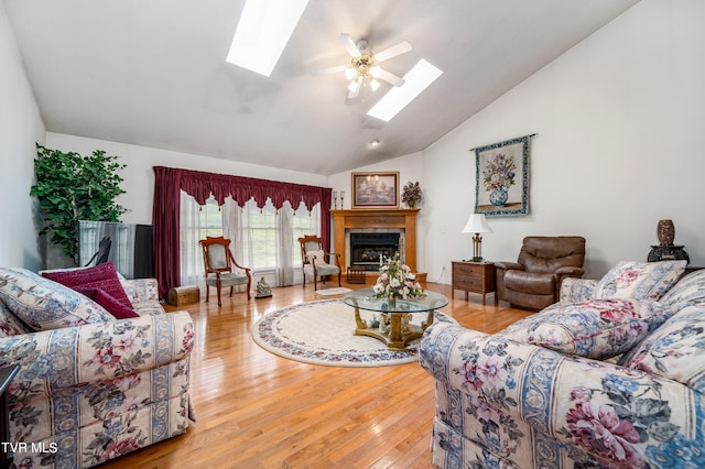 living room with a skylight, ceiling fan, high vaulted ceiling, light wood-type flooring, and a tile fireplace