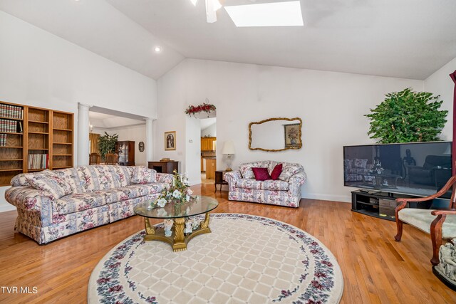 living room with a skylight, high vaulted ceiling, ornate columns, and light hardwood / wood-style flooring