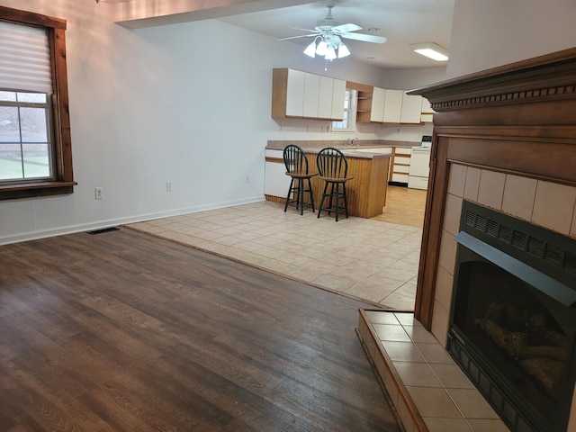 kitchen with a kitchen bar, a fireplace, white electric stove, white cabinetry, and light hardwood / wood-style floors