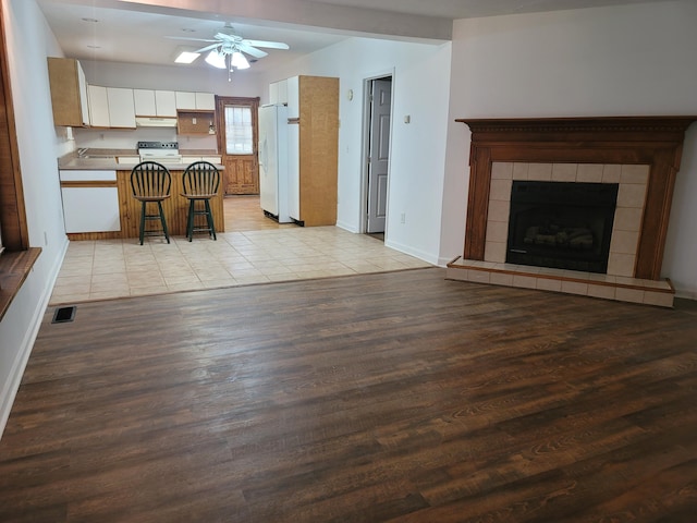 unfurnished living room with a tile fireplace, light wood-type flooring, and ceiling fan