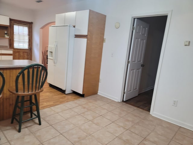 kitchen with white fridge with ice dispenser, light wood-type flooring, and white cabinets