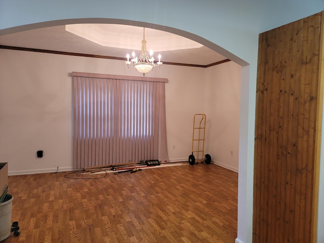 empty room featuring ornamental molding, a notable chandelier, hardwood / wood-style floors, and a tray ceiling