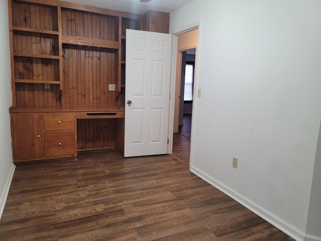 unfurnished bedroom with built in desk and dark hardwood / wood-style flooring