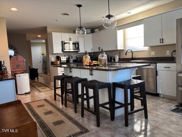 kitchen with a sink, stainless steel appliances, white cabinetry, dark countertops, and a kitchen bar