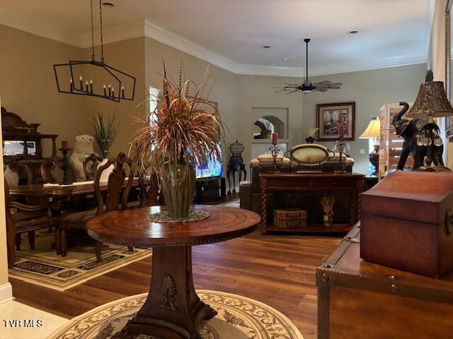 dining area featuring ceiling fan with notable chandelier, ornamental molding, and wood finished floors