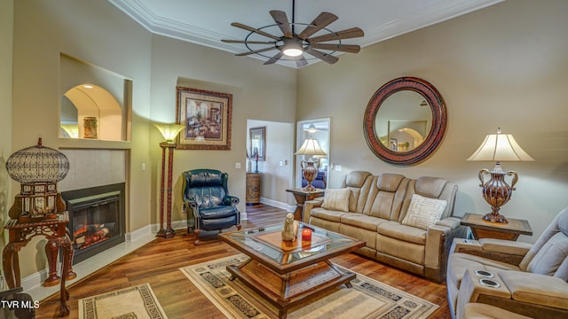 living area with a tile fireplace, wood finished floors, ornamental molding, and ceiling fan