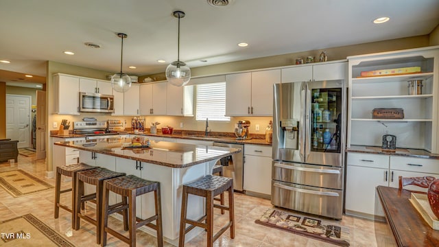 kitchen featuring a sink, a breakfast bar, dark stone countertops, stainless steel appliances, and white cabinets