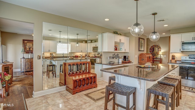 kitchen featuring a kitchen island, white cabinetry, a kitchen bar, appliances with stainless steel finishes, and dark stone countertops