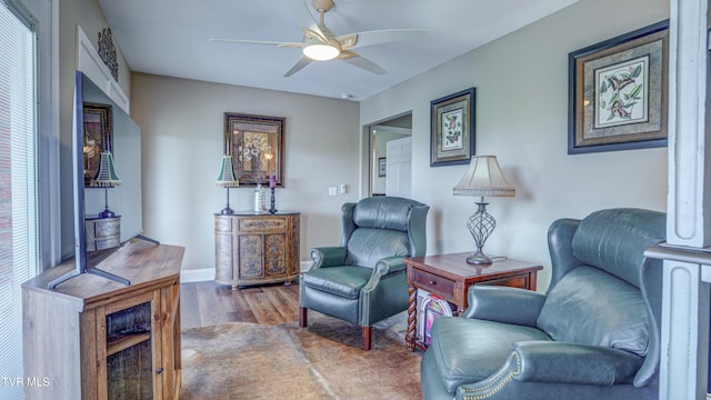living area with baseboards, wood finished floors, and ceiling fan