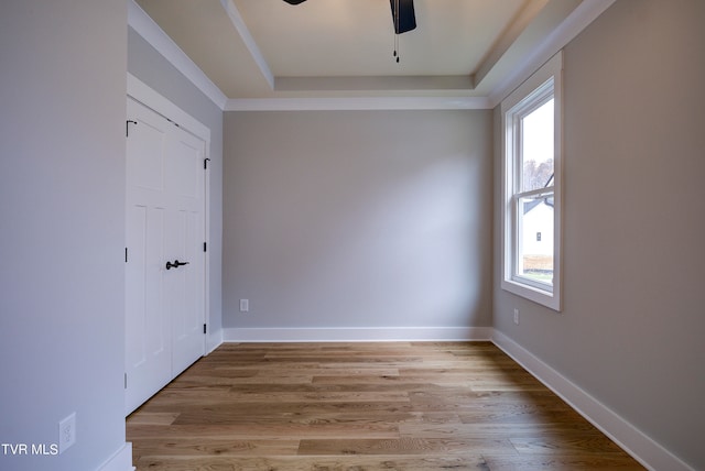 empty room with a raised ceiling, ceiling fan, and light wood-type flooring