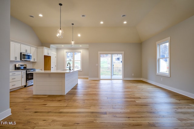 kitchen featuring appliances with stainless steel finishes, an island with sink, tasteful backsplash, and light hardwood / wood-style flooring