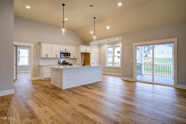 kitchen with high vaulted ceiling, appliances with stainless steel finishes, white cabinets, and light hardwood / wood-style floors