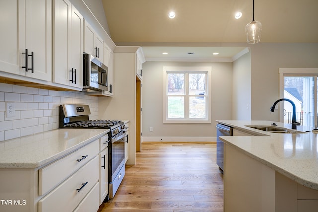 kitchen featuring light wood-type flooring, backsplash, stainless steel appliances, sink, and hanging light fixtures