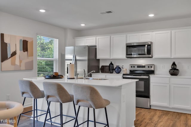 kitchen with light hardwood / wood-style floors, stainless steel appliances, a center island with sink, and white cabinetry