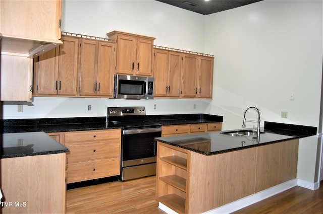 kitchen with appliances with stainless steel finishes, dark stone countertops, light hardwood / wood-style floors, and sink