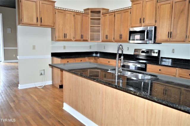 kitchen with dark stone counters, appliances with stainless steel finishes, light wood-type flooring, and sink