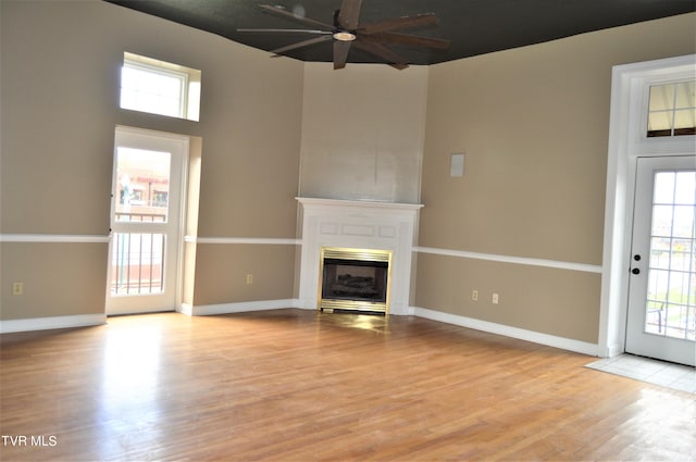 unfurnished living room featuring ceiling fan, light wood-type flooring, a wealth of natural light, and a towering ceiling