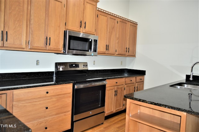 kitchen with appliances with stainless steel finishes, sink, light wood-type flooring, and dark stone countertops