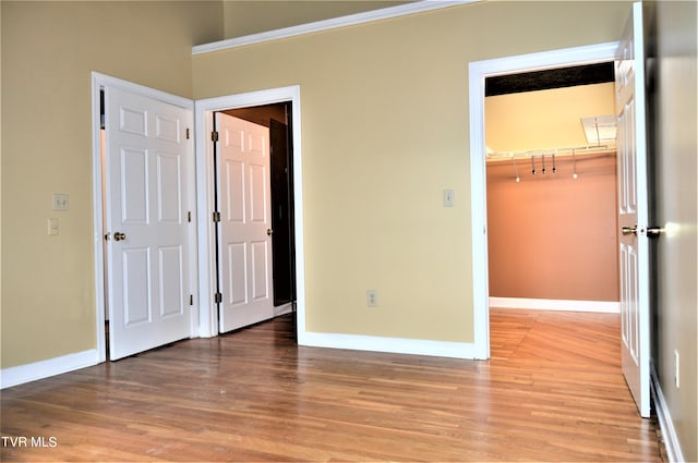 unfurnished bedroom featuring ornamental molding, a closet, light wood-type flooring, and a walk in closet