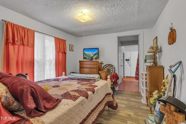 bedroom featuring a textured ceiling, white refrigerator with ice dispenser, and hardwood / wood-style floors