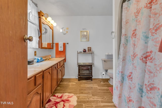 bathroom featuring double vanity, hardwood / wood-style flooring, a wood stove, and toilet