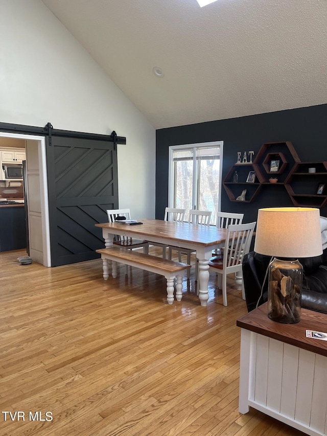 dining area with a barn door, lofted ceiling, and light hardwood / wood-style floors